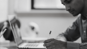 man writing notes from computer